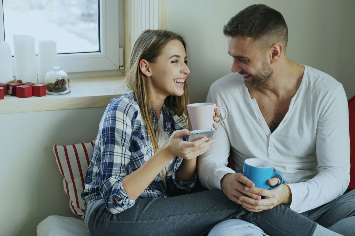 A couple shares coffee and smiles at home.