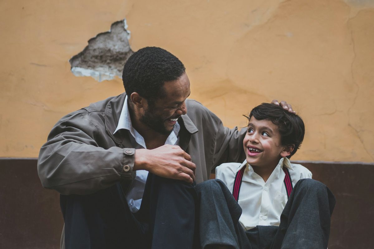 A father and his young son sit together on a step, smiling.