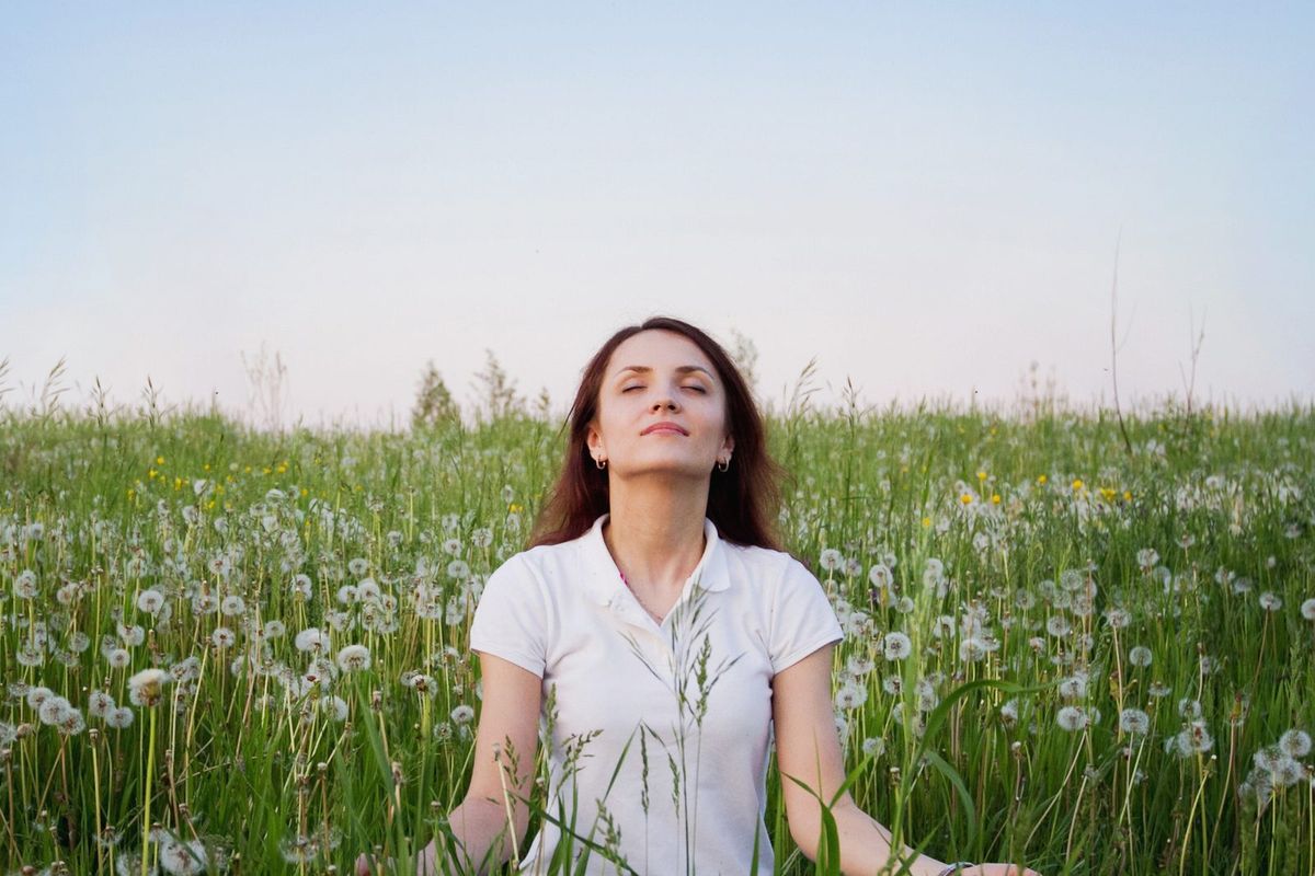 A woman sits in a green field with her eyes closed.