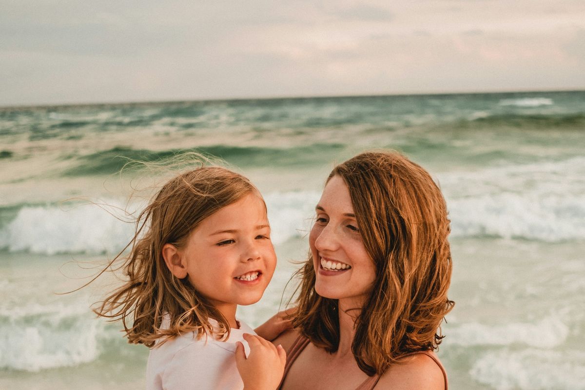 A mother holds her young daughter at the beach.