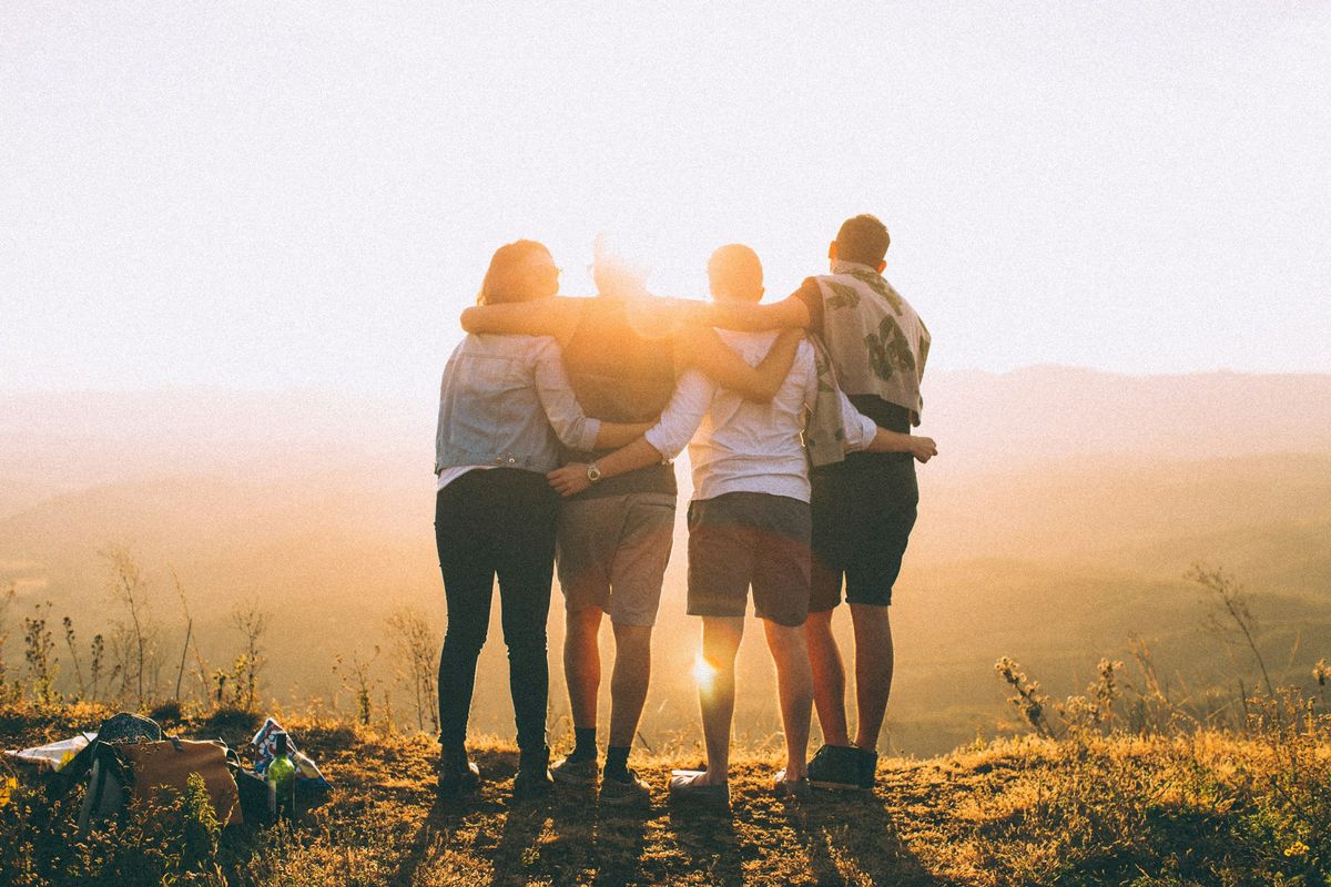 Four friends stand arm in arm at sunset.