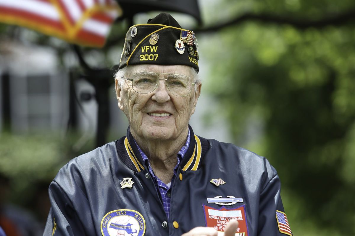 An older veteran in a VFW cap smiles outdoors.