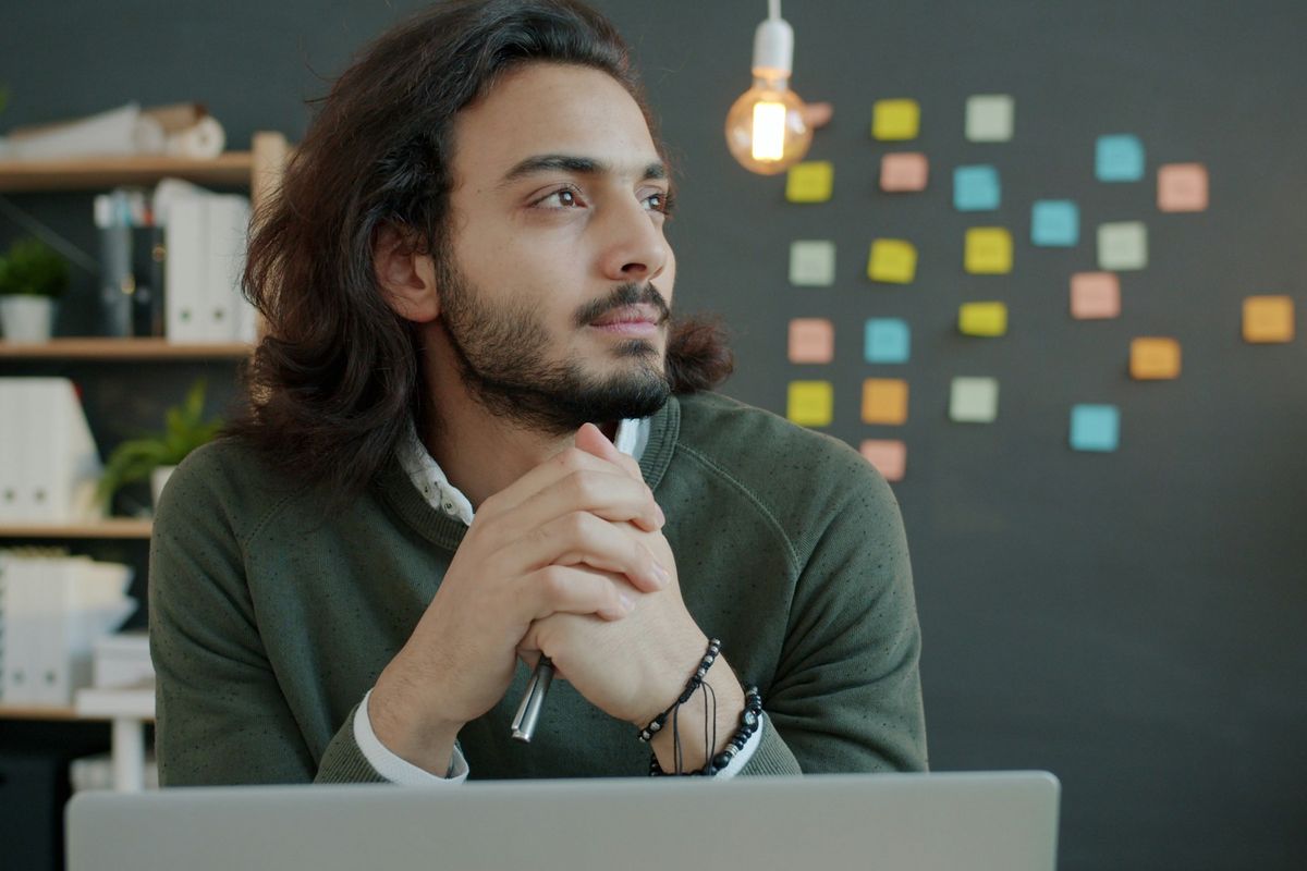 A young man sits at a desk, thinking.